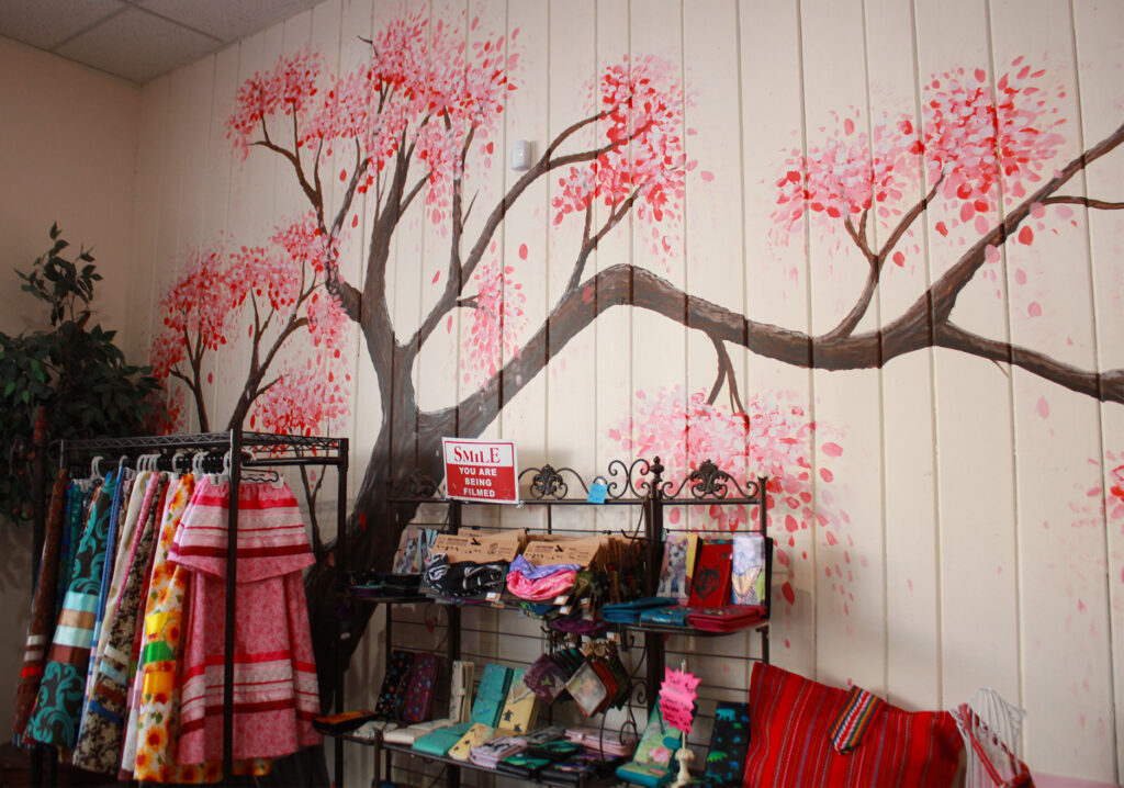 A cherry blossom tree mural with a rack in front of it filled with skirts