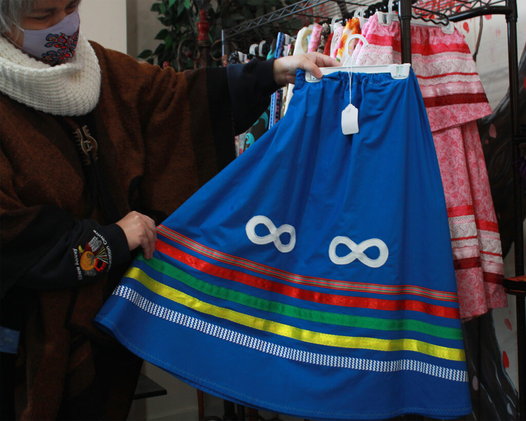 A woman holds up a ribbon skirt with the Metis infinity symbol sewn on