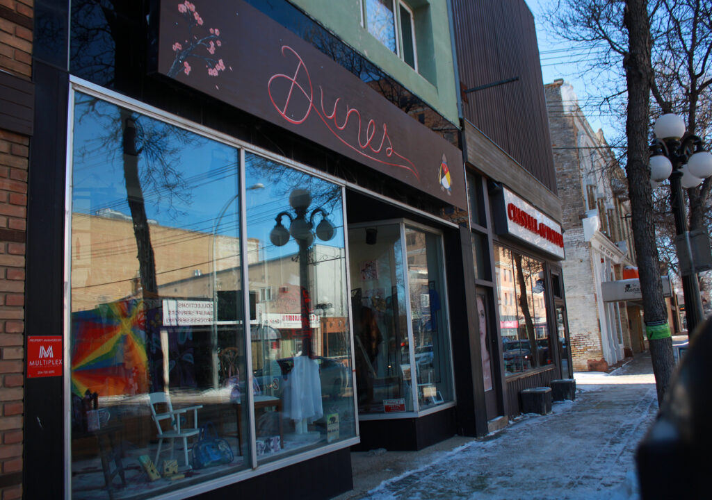 A glass storefront with merchandise in the window and a sign reading "Dunes"
