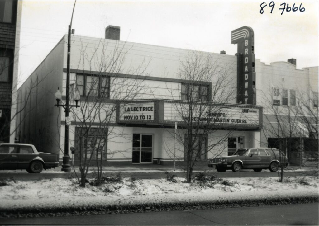 Black and white photo taken from the left of the Broadway shows the theatre with some snow and cars parked in front.